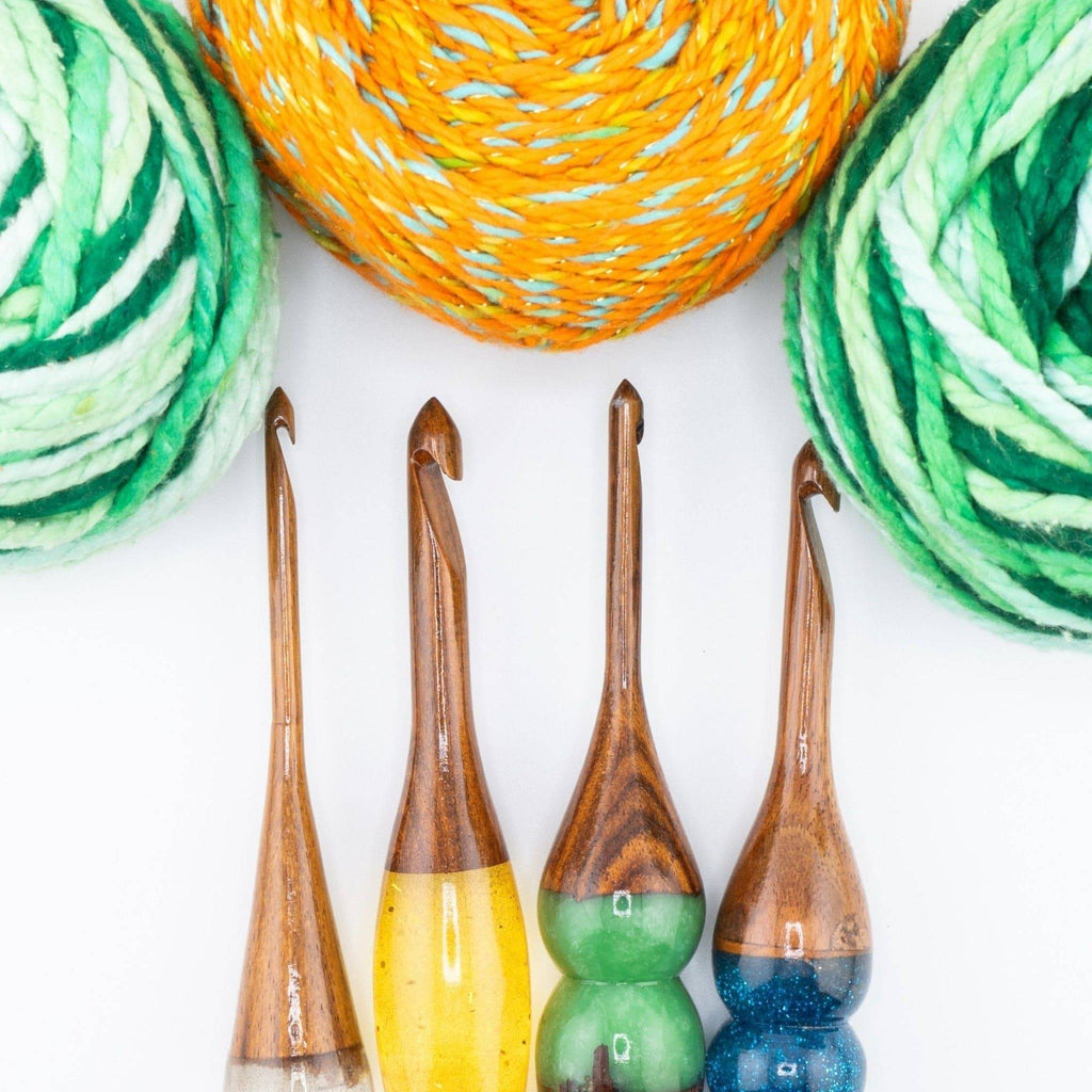 Rosewood crochet hooks with sparkly resin handles beside balls of yarn